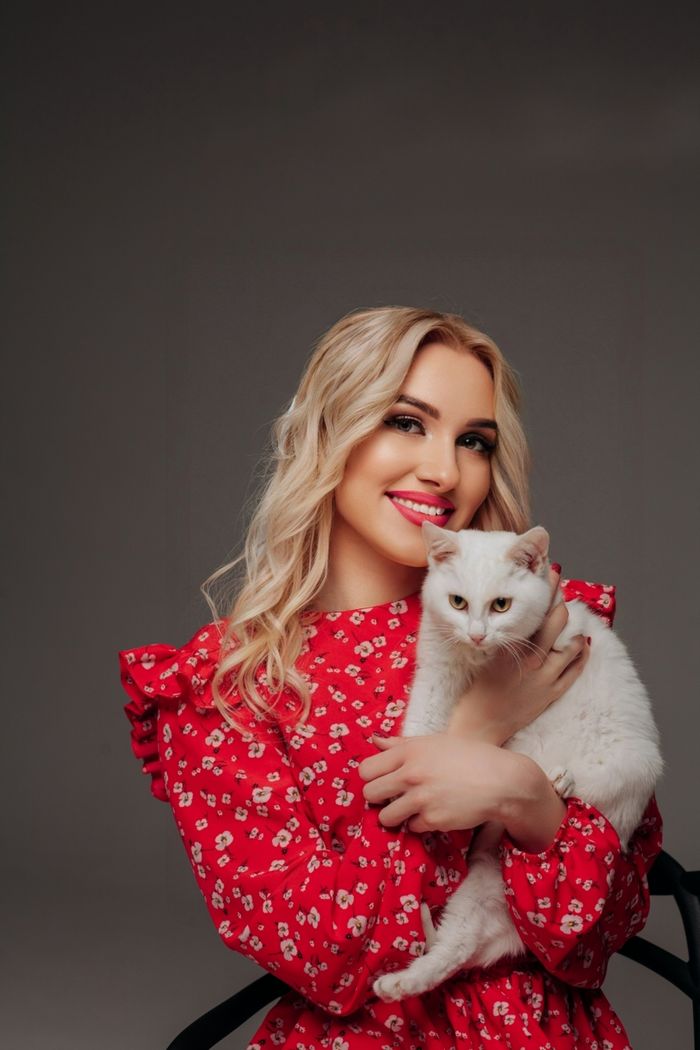 Smiling blonde woman embraces white cat in studio portrait.