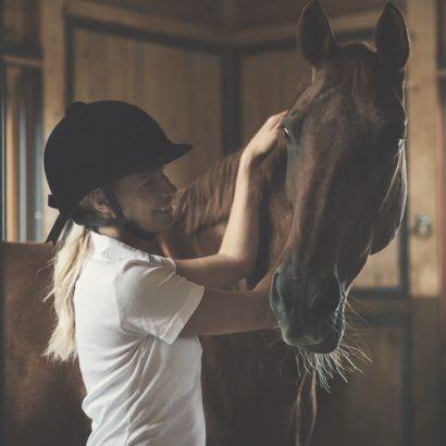 Woman in front of a barn with her horse. She is stroking him and smiling.